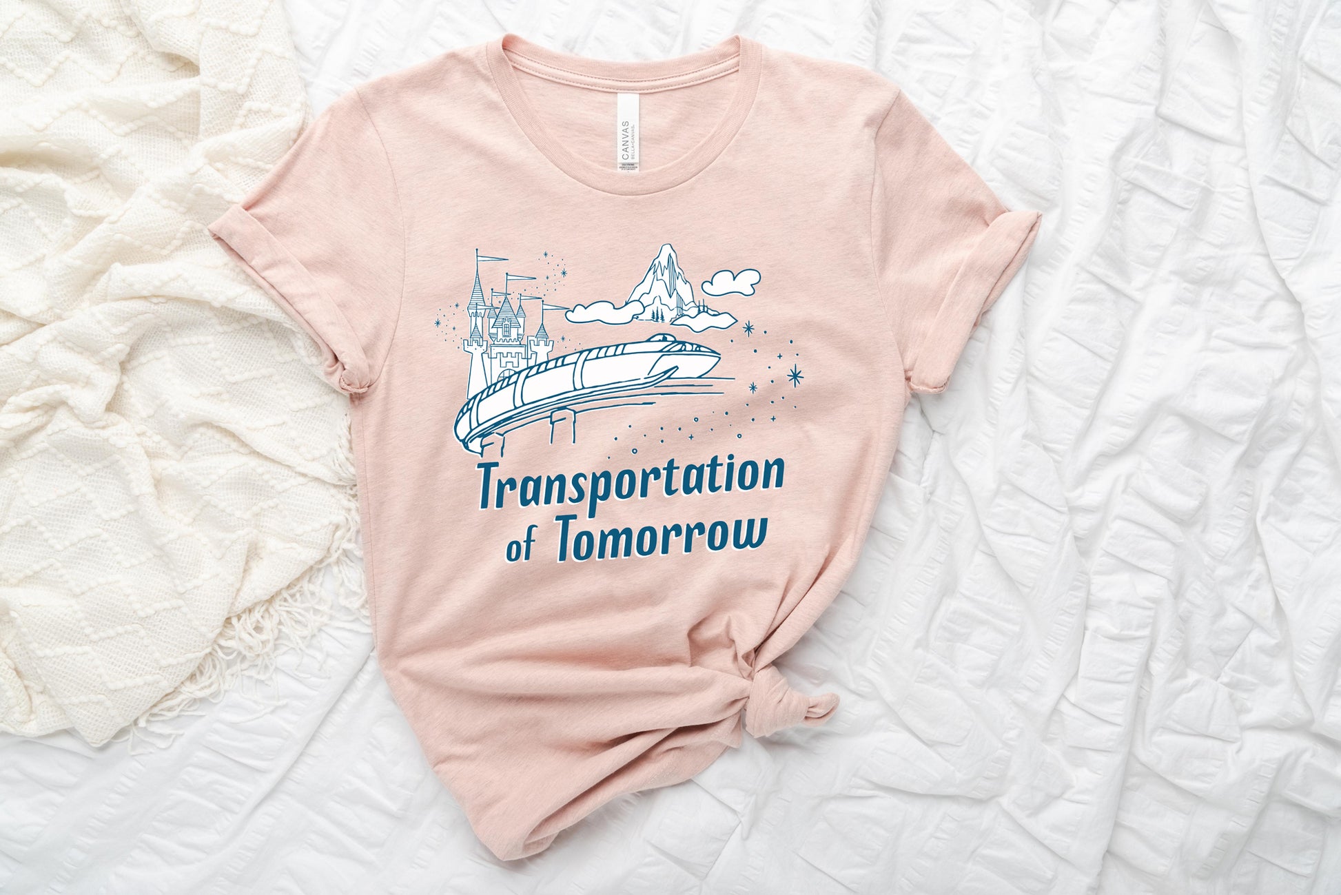 Light pink shirt printed with vintage style sketch of the Matterhorn, Castle, and Monorail with pixie dust. The shirt says Transportation of Tomorrow.